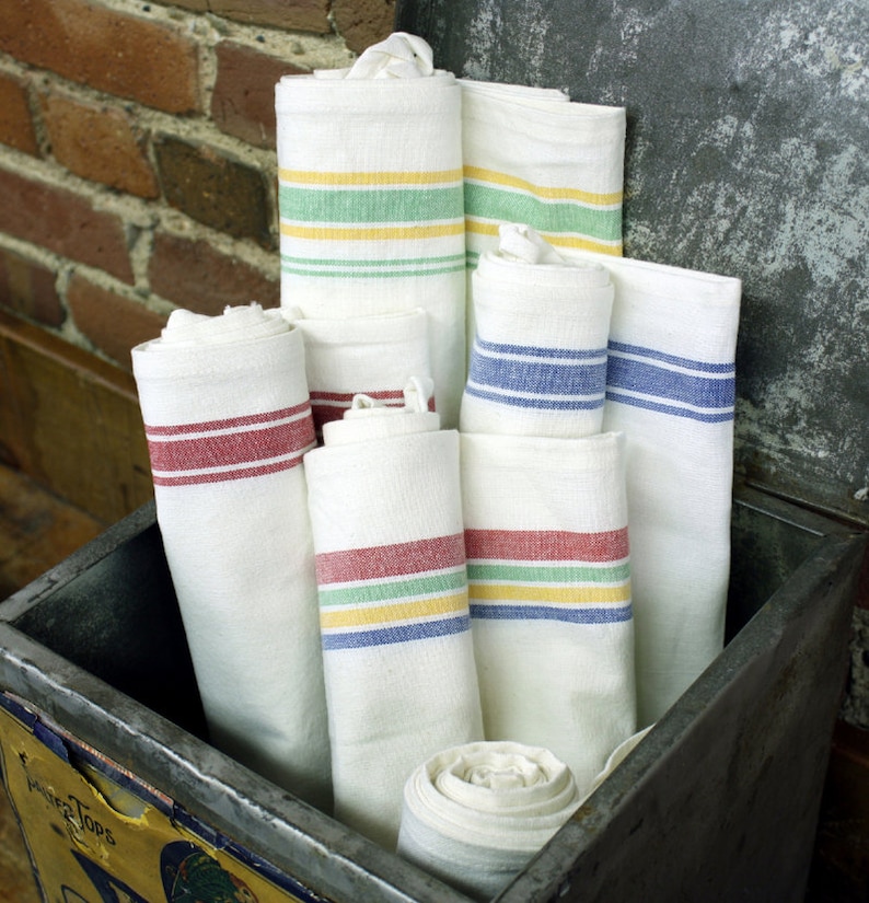 May include: A stack of white tea towels with colorful stripes. The towels are folded and stacked in a metal container. The towels have red, blue, and green stripes.