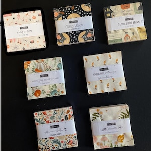 May include: Six square stacks of patterned fabric squares, each wrapped in a white paper band with a printed ruler edge. The fabric collections feature seasonal themes including Halloween motifs, pumpkins, acorns, and floral designs with various colors.