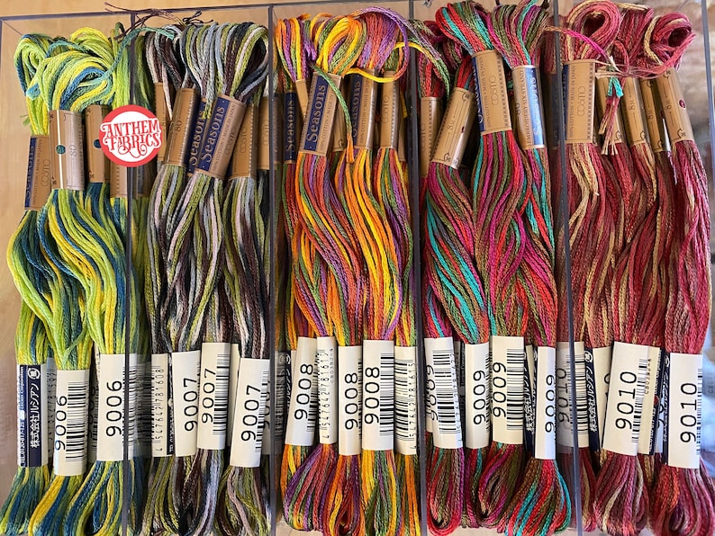 May include: A close-up of ten spools of embroidery floss, each with a different color combination. The spools are labeled with the numbers 9006, 9007, 9008, 9009, and 9010. The spools are arranged in a row, with the numbers increasing from left to right.