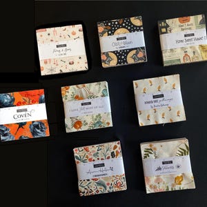 May include: Eight square fabric charm packs featuring various seasonal prints. Each stack is secured with a white paper band labeled with collection names like Potion & Boos, Owl-O-Ween, Home Sweet Haunt, Coven, I Love Fall Most of All, Pumpkin Spice Gatherings, Acorn Hollow, and Frivolity.