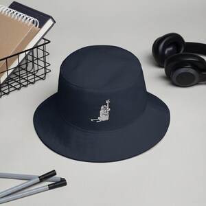 May include: A navy blue bucket hat with a white embroidered design of a monkey holding a banana.