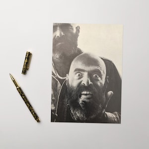 May include: Black and white photograph of two men with beards. The man in the foreground has a wide-open mouth and a surprised expression. The man in the background is partially obscured by the man in the foreground.