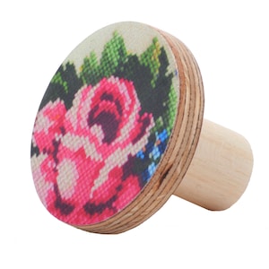 May include: A wooden bottle stopper with a round, floral design. The design features pink roses and green leaves on a white background.