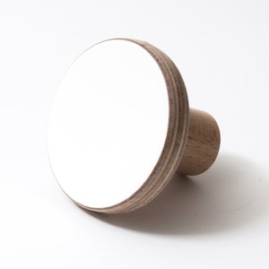 Könnte beinhalten: Ein runder, weißer Holz-Knopf mit einem braunen Holzsockel. Der Knopf ist aus Sperrholz mit einer weiß lackierten Oberfläche.