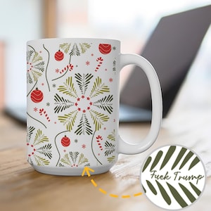 May include: White ceramic mug with a festive Christmas pattern featuring red ornaments, candy canes, and green and black fir trees. The mug has a white handle and the words "Fuck Trump" are printed on the bottom.
