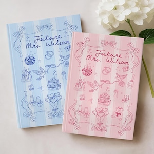 May include: Two notebooks with the text "Future Mrs. Wilson" and wedding-themed illustrations. One notebook is light blue with blue accents, and the other is pink with pink accents. Both have a striped background.