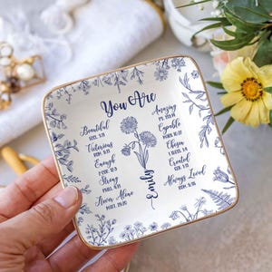 May include: A square, white ceramic trinket dish with a gold rim. The dish features blue floral designs and inspirational text, including "You Are Beautiful" and "Always Loved." The name "Emily" is also displayed.