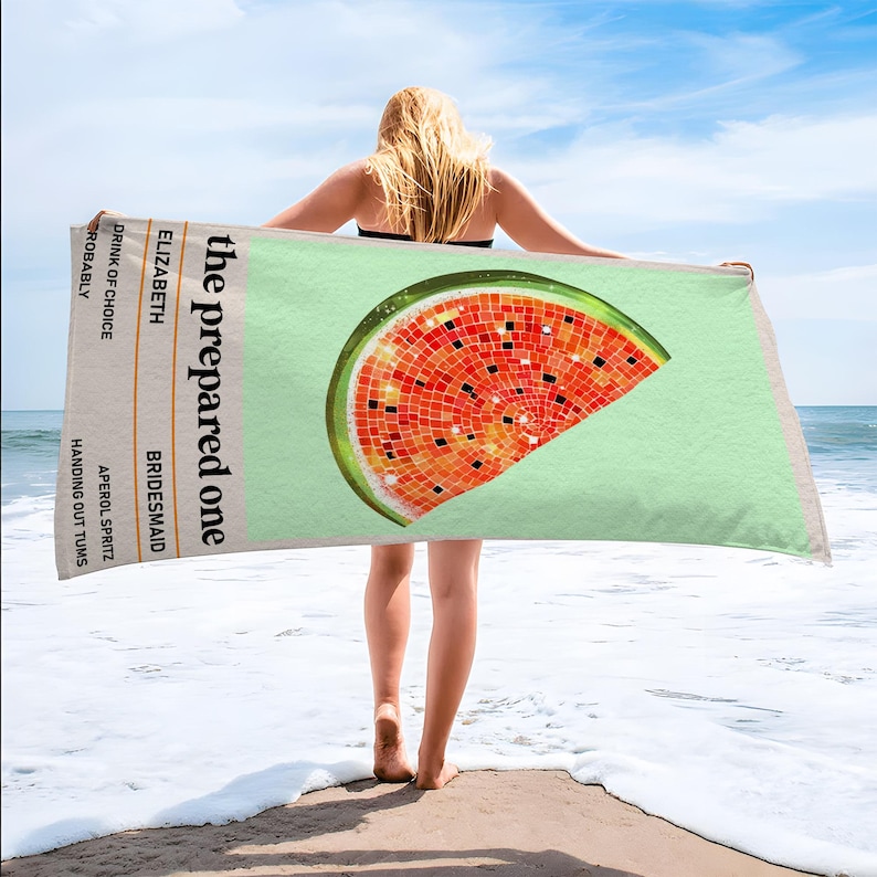 May include: A beach towel with a watermelon slice design. The towel has a light green background and a mosaic-style watermelon slice in red, orange, and black. Text on the towel reads "the prepared one" and "Elizabeth, Bridesmaid".