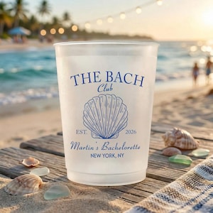 May include: A frosted plastic cup featuring blue text and a seashell graphic. The text reads THE BACH CLUB, EST. 2026, Martin's Bachelorette, and NEW YORK, NY. The design is centered on the front of the cup, which has a smooth, translucent finish.