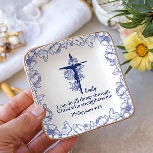 May include: Square, white ceramic trinket dish with a blue floral border and gold trim. The centre features a blue cross design with the name "Emily" and the text "I can do all things through Christ who strengthens me Philippians 4:13."