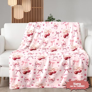 May include: Pink and white fleece throw blanket with a repeating pattern of pink bows, red cherries, and the name "Sophia" printed on it. The text "Name can be CHANGED" is printed in the bottom right corner.
