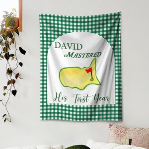 May include: A white tapestry with a green and white checkered border. The center features a white circle with the text "DAVID MASTERED His First Year". Inside the circle is a yellow and green golf course design with a red flag.