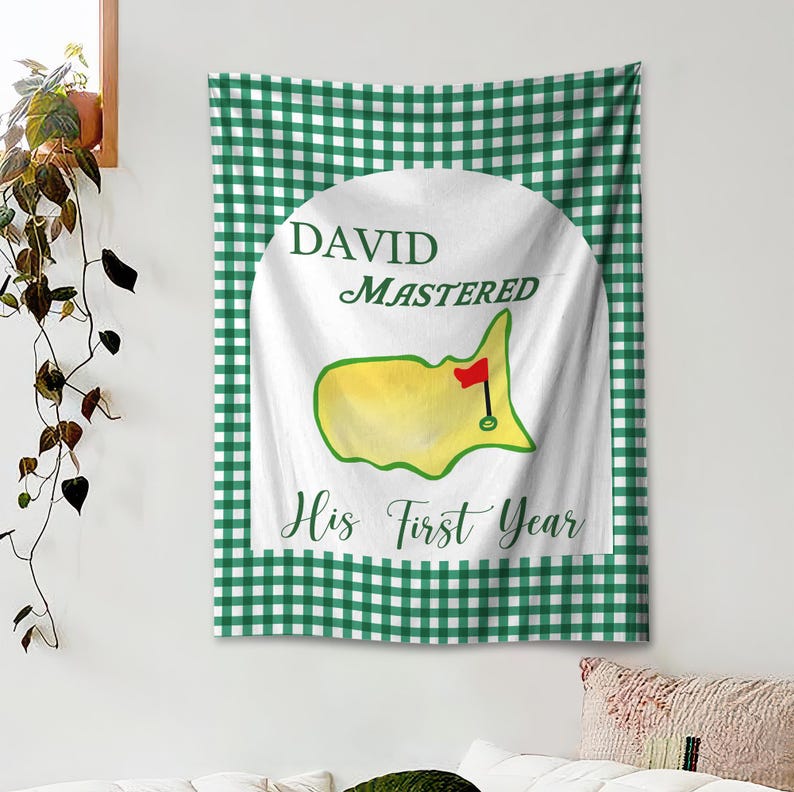 May include: A white tapestry with a green and white checkered border. The center features a white circle with the text "DAVID MASTERED His First Year". Inside the circle is a yellow and green golf course design with a red flag.