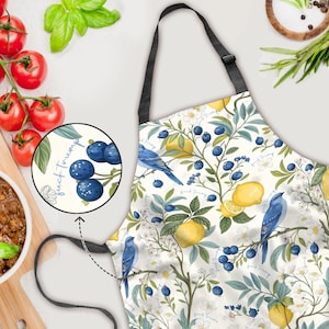 May include: Apron with a botanical design featuring lemons, blueberries, and blue birds on a cream background. The apron has a black neck strap and a small circular inset with blueberries and the text "fuck Trump".