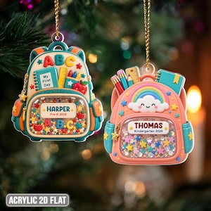 May include: Two backpack-shaped ornaments hanging by gold cords. The left one is teal and cream with 'HARPER Pre-K 2026' and 'ABC' text. The right one is peach and teal with a rainbow, 'THOMAS Kindergarten 2026' text, and shaker-style glitter.