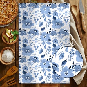 May include: White kitchen towel with a blue floral pattern and the text "Fuck Trump" repeated throughout. The design features watercolor-style flowers and leaves. The towel is rectangular and likely made of cotton or a similar absorbent material.