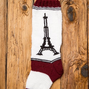 May include: A white knitted Christmas stocking with a burgundy cuff and a black and white Eiffel Tower design.