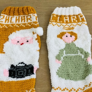 May include: Two knitted Christmas stockings, one with a Santa Claus design and the other with a woman in a green dress. The stockings are white with gold accents and the text "HO HO HO" and "JINGLE" is visible.