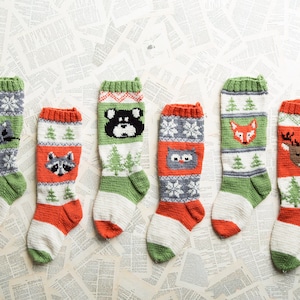 Può includere: Sei calze di Natale lavorate a maglia con disegni di animali. Ogni calza presenta un animale diverso: un procione, un orso, un gufo, una volpe e un cervo. Le calze hanno sezioni verdi, bianche e rosse con motivi a fiocco di neve e alberi.