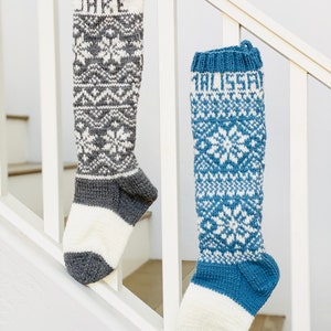 Peut inclure: Deux chaussettes de Noël en tricot avec des motifs de flocons de neige, l'une grise et blanche, l'autre bleue et blanche, avec les noms "Jake" et "Alyssa" brodés dessus.
