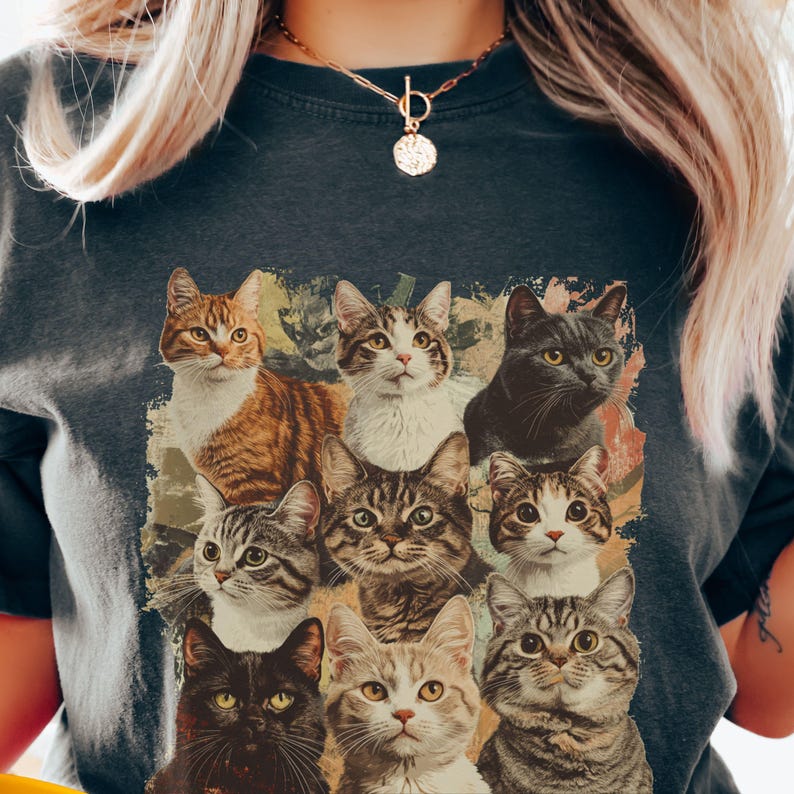 K&ouml;nnte beinhalten: Ein dunkelgraues T-Shirt mit einem Vintage-Druck von neun Katzen in verschiedenen Posen. Die Katzen sind in Braun-, Schwarz- und Wei&szlig;t&ouml;nen gehalten.