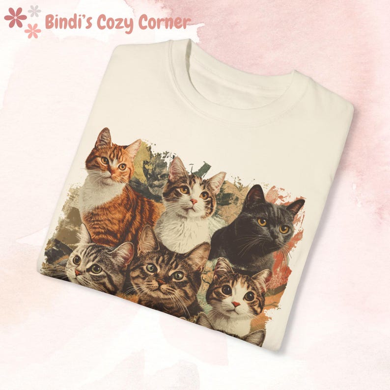 K&ouml;nnte beinhalten: Ein wei&szlig;es T-Shirt mit einem grafischen Druck von sechs Katzen. Die Katzen sind in einer Gruppe angeordnet, wobei ihre K&ouml;pfe und Schultern sichtbar sind. Die Katzen sind alle in verschiedenen Farben und Mustern, darunter braunes Tabby, Schwarz, Wei&szlig; und Calico.