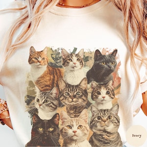 K&ouml;nnte beinhalten: Ein wei&szlig;es T-Shirt mit einem Vintage-Druck von neun Katzen in verschiedenen Posen. Die Katzen sind alle in verschiedenen Farben und Mustern gehalten und in einem gitterartigen Muster angeordnet. Der Hintergrund des Drucks hat einen verblassten, abgenutzten Look.