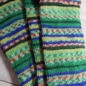 May include: A pair of knitted socks with a colorful pattern. The socks feature horizontal stripes in shades of green, blue, yellow, and red. The design includes small, repeating patterns and a textured appearance, suggesting a handmade or artisanal quality.