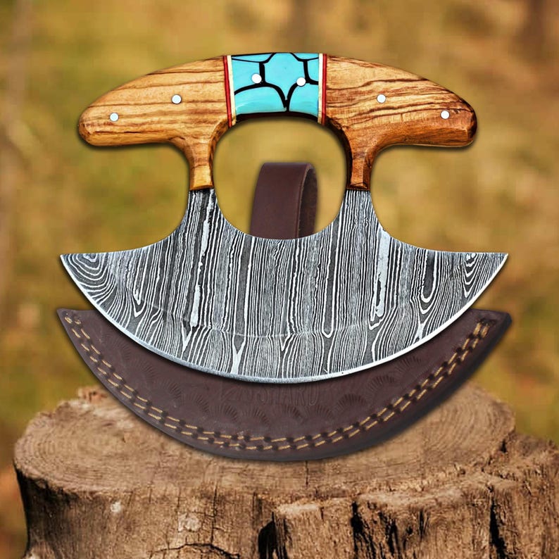 May include: A curved, double-edged knife with a wooden handle and a turquoise inlay. The knife has a damascus steel blade and comes with a brown leather sheath.