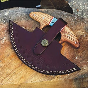 May include: A brown leather sheath with a decorative stitching pattern and a brass button. Two knives with wooden handles are secured inside the sheath.