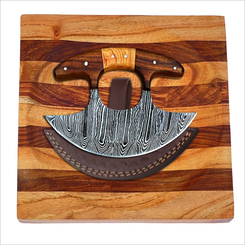 May include: A curved, stainless steel cleaver with a wooden handle and a leather sheath, resting on a wooden cutting board with a striped pattern.