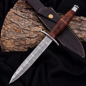 May include: A handcrafted dagger with a patterned steel blade and a brown leather-wrapped handle. The dagger is accompanied by a dark brown leather sheath with a brass button closure. The blade has a unique swirling pattern.