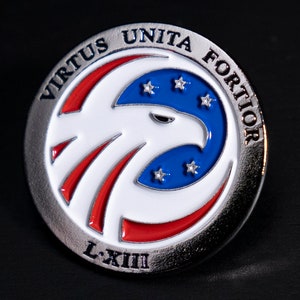 May include: A silver pin with a red, white, and blue eagle design. The eagle is surrounded by a circle with the words "Virtus Unita Fortior" and "L-XII" in silver lettering.