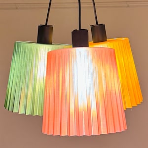 May include: Three hanging light fixtures with pleated shades in green, orange and yellow.