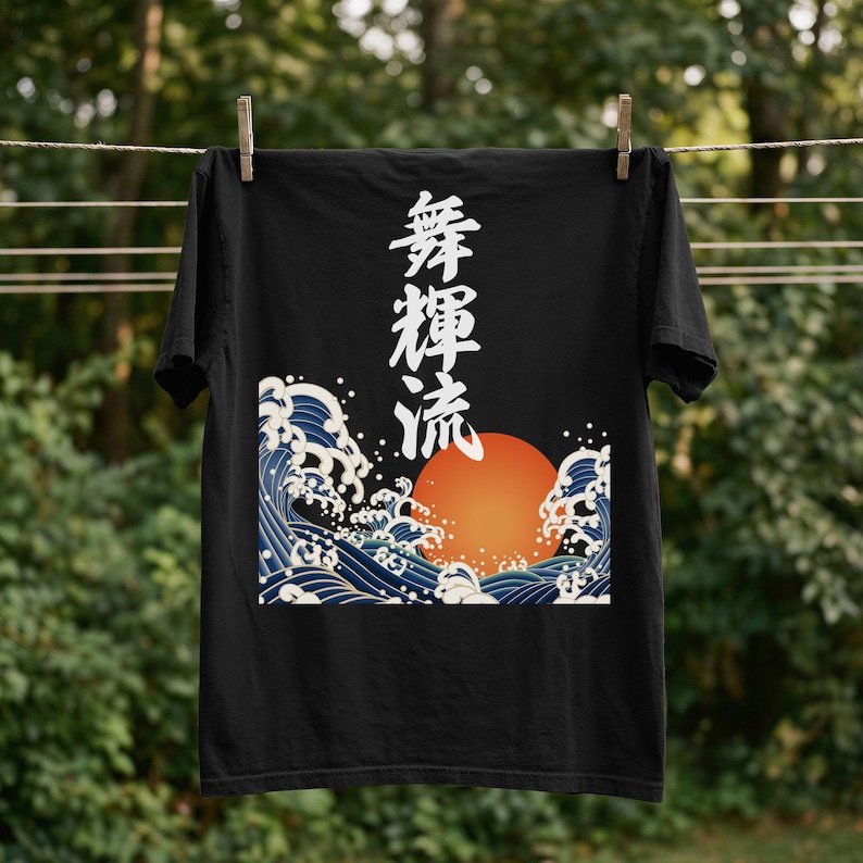 A black t-shirt hangs on a clothesline outdoors with wooden clothespins. A forest is blurred in the background. The dramatic ukiyo-e style design on the t-shirt features a glowing orange sun and tumultuous blue waves. Black Japanese kanji script meaning "Infinite Flow" is printed vertically.