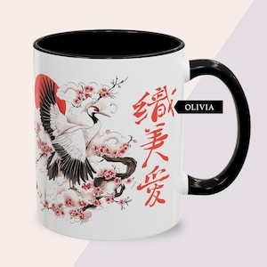 May include: White ceramic mug with a black interior and handle. The mug features a crane design with a red sun, cherry blossoms, and Japanese characters. The name "OLIVIA" is printed on the side.