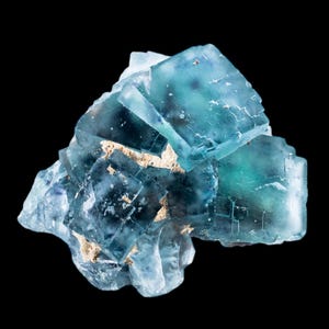May include: A close-up of a fluorite crystal cluster. The crystal features a mix of blue and green hues with a translucent appearance. The crystal has a cubic structure with visible facets and is set against a black background.