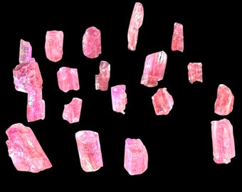 Puede incluir: Una colección de pequeños fragmentos de cristal rosa translúcido dispersos por el encuadre. Cada pieza muestra bordes irregulares y dentados, con formas geométricas variadas y un tono rosa brillante con una textura superficial vítrea.