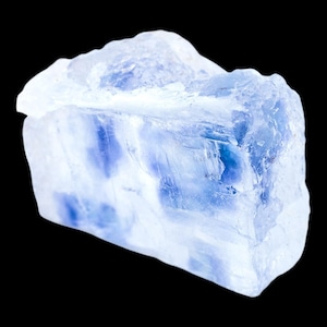 May include: A translucent, light blue crystal with darker blue inclusions. The rough-cut stone has a crystalline structure and is set against a black background. The crystal's surface reflects light, highlighting its natural texture.