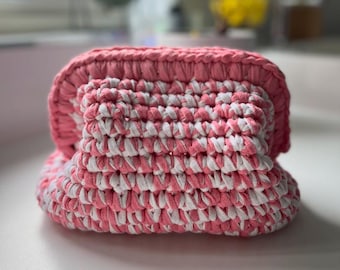 May include: A handmade, pink and white crocheted basket. The basket is made with thick yarn, creating a textured appearance. The color scheme is a combination of light pink and white, with the white yarn woven in a pattern.
