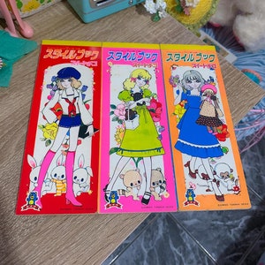 May include: Three colorful paper doll books with the text "スタイルブック スイートコ" on the front. Each book features a different doll with a different outfit and accessories. The dolls are surrounded by cute animals.