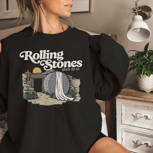 May include: Black sweatshirt with a graphic of a stone tomb with a cross and the text "Rolling Stones Since AD 33".