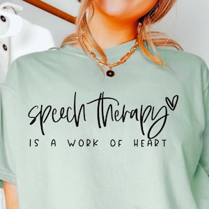 May include: A light green t-shirt with the text "Speech Therapy is a work of heart" in black script with a small heart symbol.