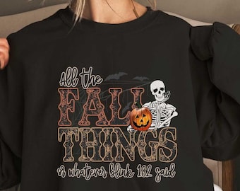 May include: Black sweatshirt with the text "All the Fall Things or whatever blink 182 said." The design includes a jack-o'-lantern and a skeleton. The text is in orange and brown, with a spiderweb design.