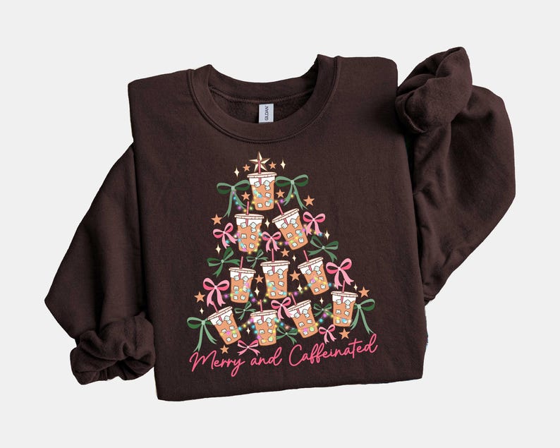 May include: A dark brown sweatshirt with a Christmas tree design made of coffee cups, bows, and lights. The text "Merry and Caffeinated" is written in pink script at the bottom of the tree.