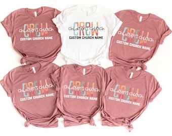 May include: A collection of t-shirts in various shades of pink and one white shirt. Each shirt features the text "CREW", "children's church", and "CUSTOM CHURCH NAME" in a colorful, retro font. The shirts are likely for a children's church group.