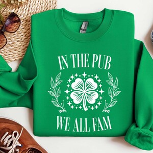 May include: Green sweatshirt with white text that reads "In the Pub We All Fam" and a white four-leaf clover graphic.