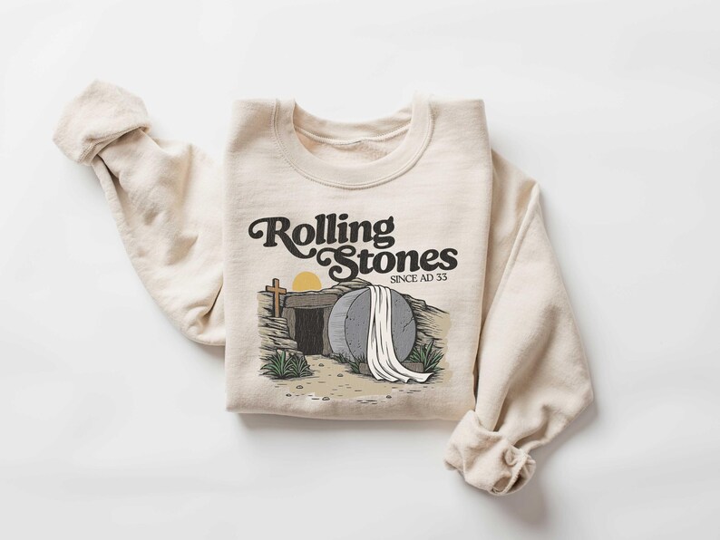 May include: A beige sweatshirt with a graphic print of a stone tomb with a white sheet on top. The text "Rolling Stones Since AD 33" is printed above the image.