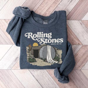 May include: A dark blue sweatshirt with a graphic of a stone tomb with a rolling stone and the text "Rolling Stones Since AD 33".