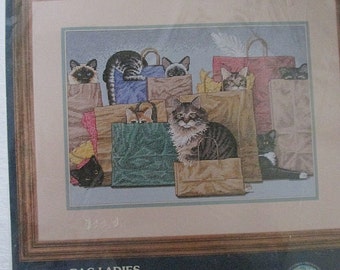 May include: Cross-stitch pattern featuring a group of cats peeking out of shopping bags. The title "BAG LADIES" and the designer's name "Braidt Braids" are printed below the image.